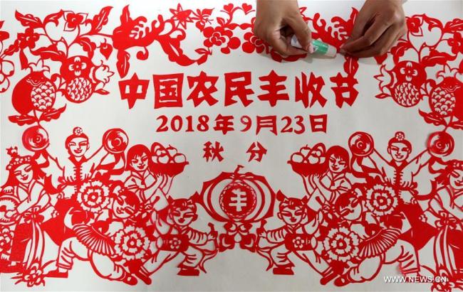 L'artiste spécialiste du papier découpé, Qiu Ting, et son mari Qiu Hanping, regardent une oeuvre sur le thème de la récolte chez eux, à Tengzhou, ville de la province chinoise du Shandong (est), le 17 septembre 2018. Mme Qiu a passé plus de deux mois pour créer cette oeuvre en papier découpé d'une longueur de 2.018 centimètres à l'approche de la première fête de la récolte des agriculteurs chinois, qui tombera pendant l'équinoxe d'automne, soit le 23 septembre prochain. (Photo : Song Haicun)