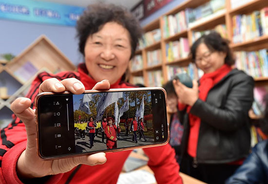Le 12 novembre 2020, une dame montre les vidéos qu'elle a réalisées avec son portable, une technique qu'elle a maîtrisée récemment, dans la bibliothèque communautaire Xinsheng de l'arrondissement de Hanjiang de la ville de Yangzhou de la province du Jiangsu (dans l'est de la Chine). (Zhuang Wenbin/ Pic.people.com.cn)<br>