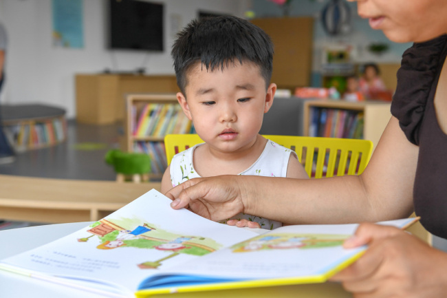 Ένα παιδί ακούει καθώς του διαβάζουν ένα εικονογραφημένο βιβλίο στο παράρτημα βιβλίων της Πινγκγιάνγκ που ανήκει στην Παιδική Βιβλιοθήκη της Τσανγκτσούν, στην επαρχία Τζιλίν της βορειοανατολικής Κίνας, στις 2 Ιουλίου.<br>Το παράρτημα, που άνοιξε στις 30 Ιουνίου, είναι η πρώτη βιβλιοθήκη εικονογραφημένων βιβλίων για παιδιά στην Τσανγκτσούν. Στεγάζει σχεδόν 5.000 βιβλία για δημόσια χρήση. [Φωτογραφία / Xinhua] 