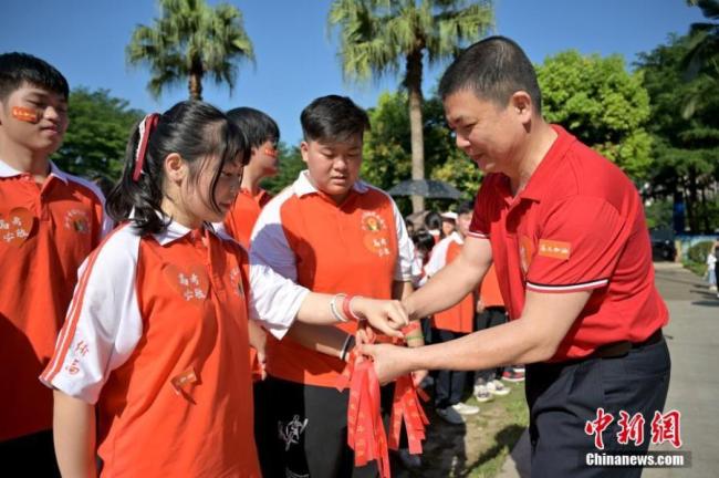 Ένας καθηγητής δένει κόκκινες κορδέλες στους εξεταζόμενους με τις καλύτερες ευχές στο Πειραματικό Λύκειο της Νανίνγκ Nanning στην Γκουανγκσί, στις 6 Ιουνίου 2021. (Φωτογραφία / Yu Jing)