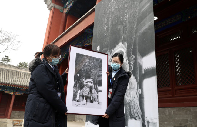 Εργαζόμενες της διοίκησης του Πάρκου των Ερειπίων Γιουανμινγκγιουάν κρατούν μια φωτογραφία από τη δεκαετία του 1920 με ένα άγαλμα του Μποτισάτβα, μιας βουδιστικής θεότητας, στο ναό Τζενγκζουέ στο Πεκίνο. [Φωτογραφία: Zou Hong / China Daily]